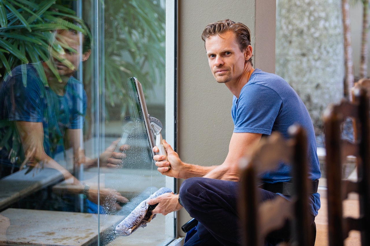 Man looking to the camera with cleaning tools in front a window