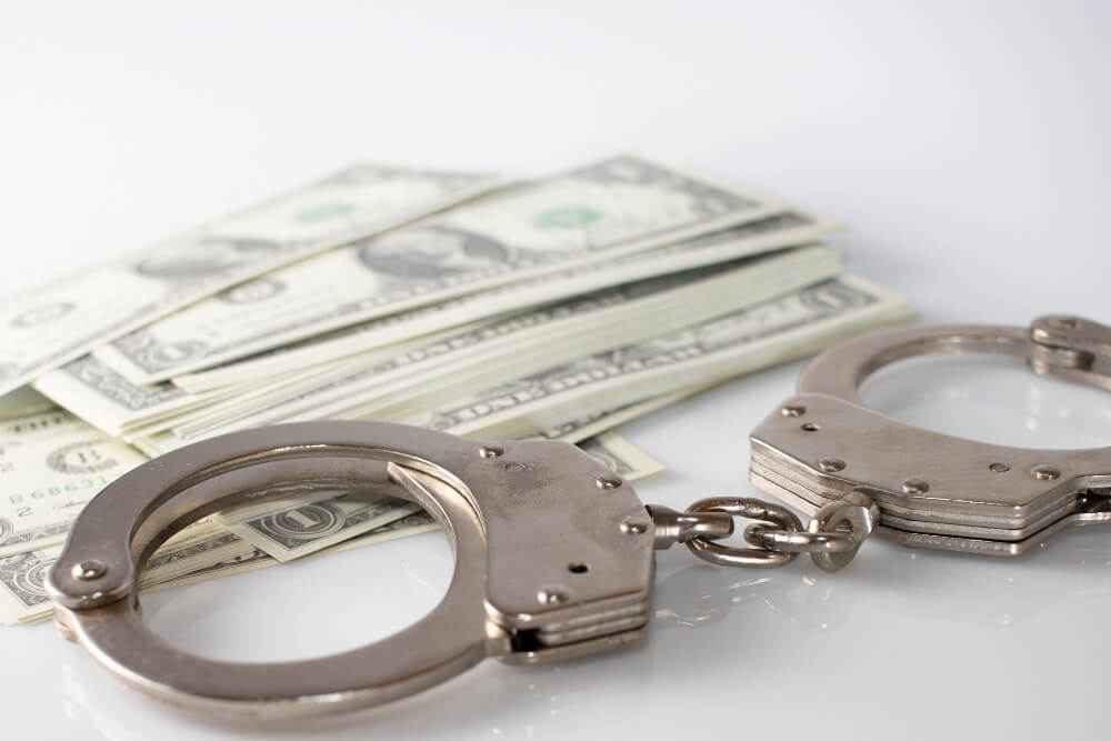 High angle shot of metal handcuffs and some dollar bills on a white surface