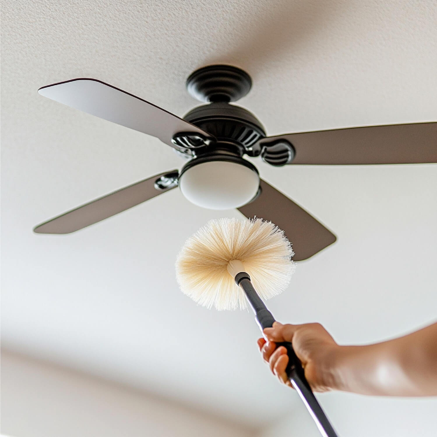 A person using a duster to clean ceiling fans and light fixtures